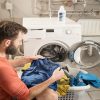 Man sitting in front of washing machine with clothes in laundry basket